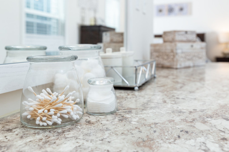 Beige marble-style countertop in a manufactured home bathroom with glass jars containing cotton swabs,  cotton balls and cotton pads and a tray with jars.