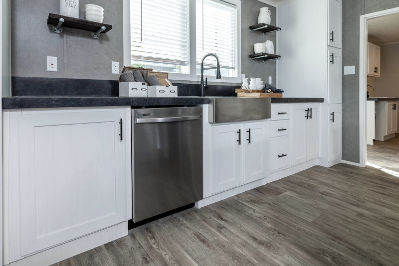 A stainless steel Samsung dishwasher in the kitchen of a Clayton manufactured home, with gray flooring and walls and white cabinets.