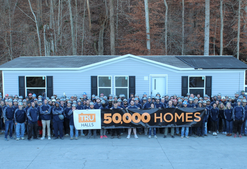 Group stands in front of home holding sign that reads "TRU Halls 50,000 Homes"