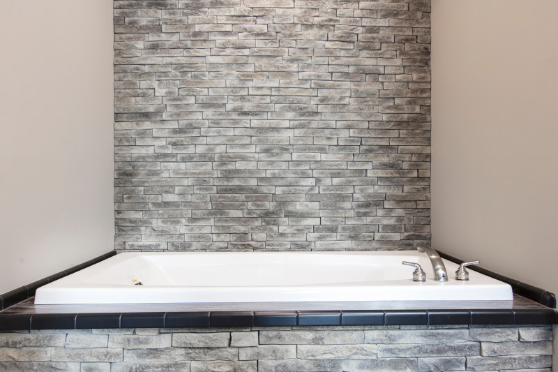 A large bathtub in a manufactured home surrounded by stone on all sides and stone accent wall behind it.