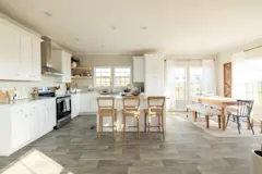 A kitchen with all white cabinets and counters and a large kitchen island that opens up into a dining area with large windows and a long wooden table with benches and chairs for seating.