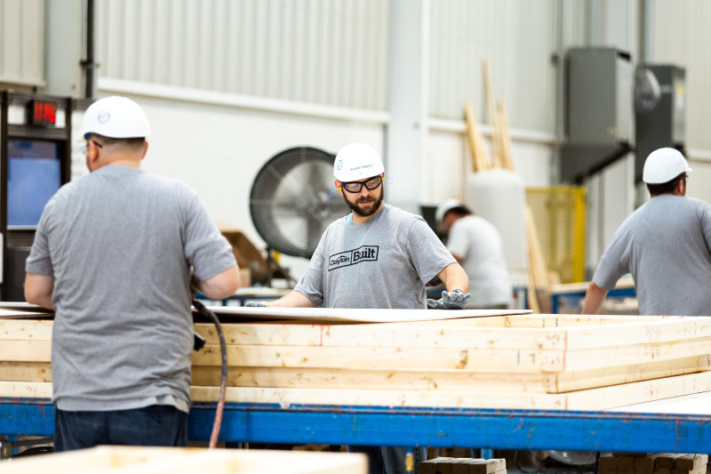 Team members in white hard hats and gray shirts work on a manufactured home inside of a Clayton home building facility