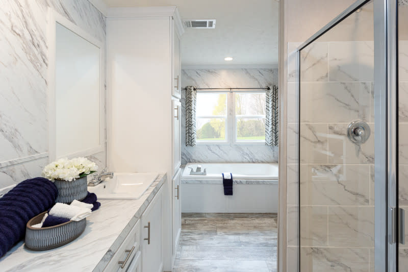 A white bathroom in a manufactured home with a double-sink vanity, a glass shower and separate soaking tub.