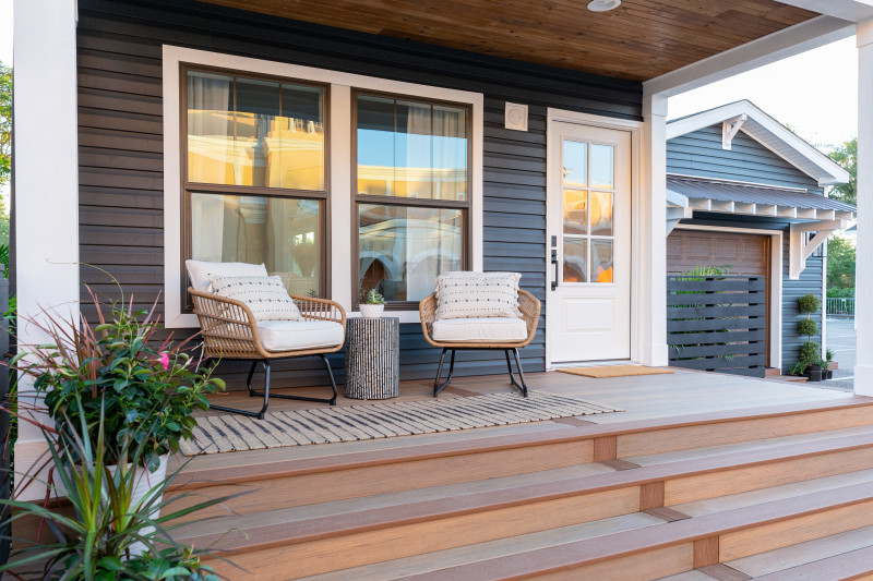Exterior of a manufactured home porch with chairs and table, with wood floor, dark siding and white trim.