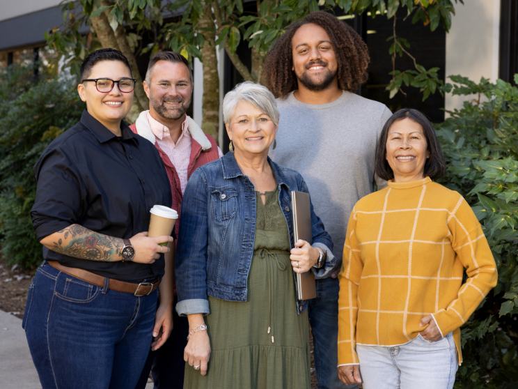 Five Clayton team members pose in front of greenery.