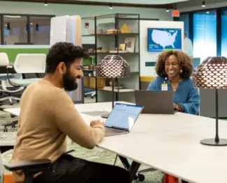 A man and woman sit across from each other with laptops at a table inside of the Clayton office.