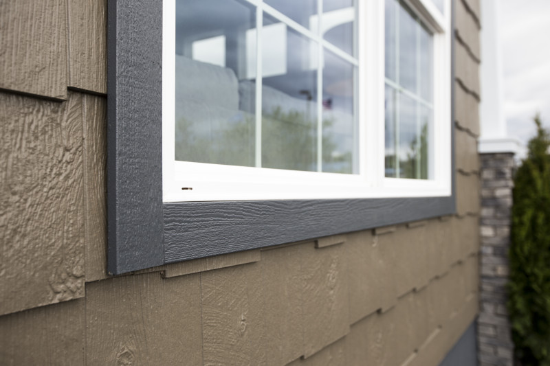 Detail shot of brown siding on a manufactured home, with a white window with grayish brown trim.