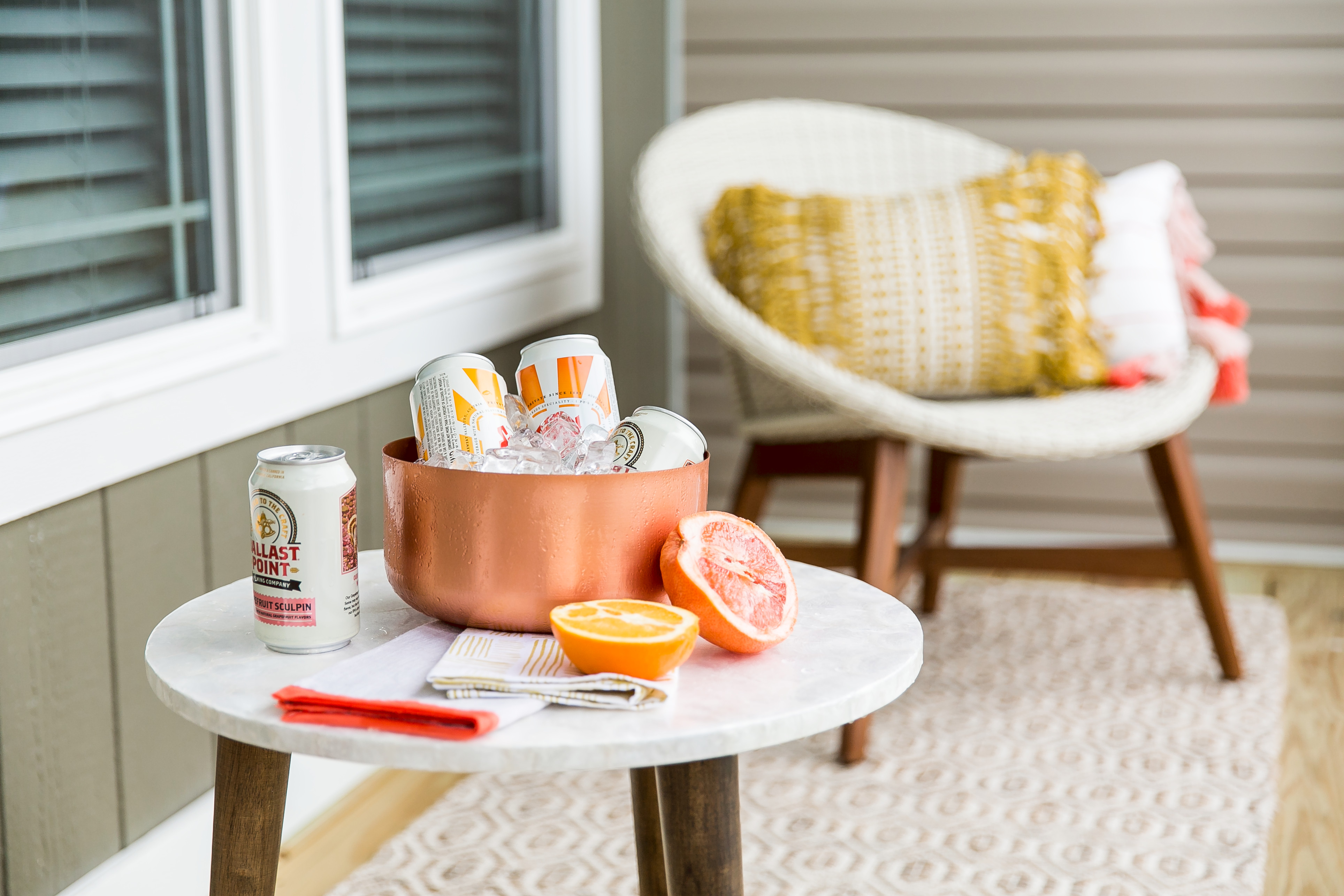 Sodas in an ice bucket with sliced citrus fruit on a porch table.