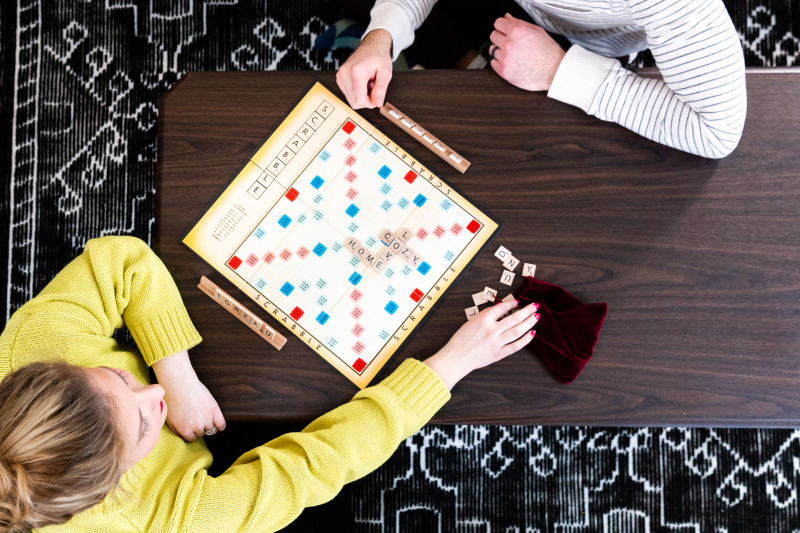 A young couple plays a word based board game on a wooden coffee table.