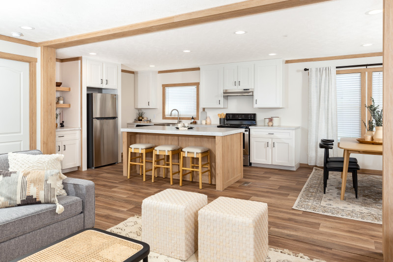 Interior of a Clayton manufactured home kitchen with light wood trim, floors and island with white cabinets and stainless steel appliances.