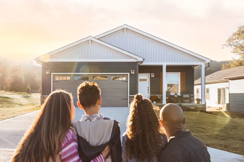 A family stands outside their Clayton home, with a sunrise in the background.