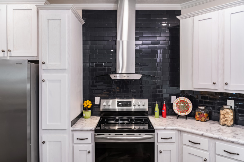 A kitchen in a manufactured home with black subway tile backsplash and white cabinets