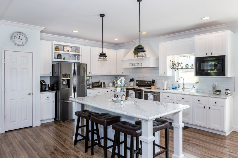 Farmhouse kitchen with white subway tile, white cabinets with black hardware, marble countertops, stainless steel appliances and white range hood.