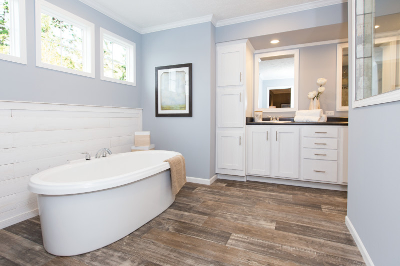 master bathroom with drop in soaker tub, blue walls, white tile accent wall and white cabinets