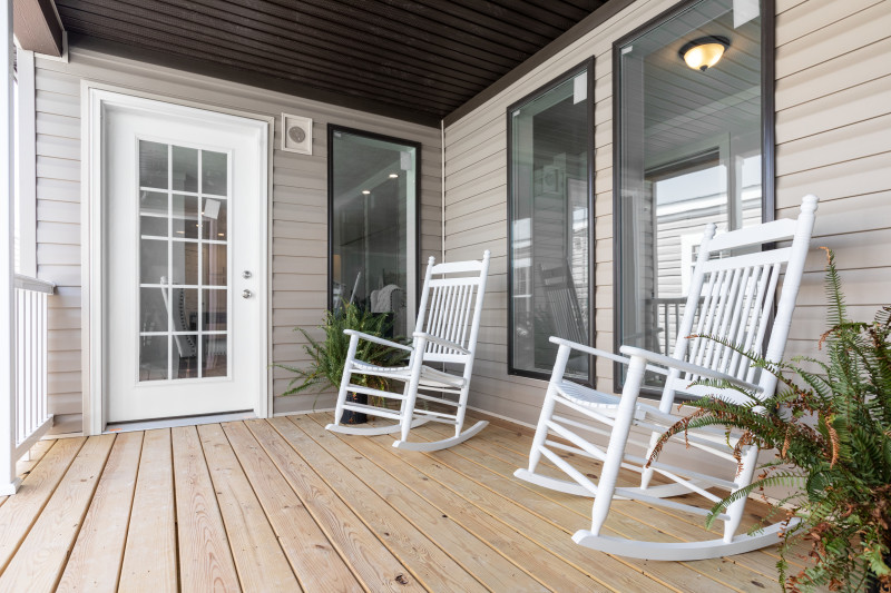 A small porch area is in view with large windows looking into the home. There are two white rocking chairs and some plants on the porch, too.