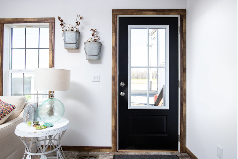 A black front door inside a home has a paned glass window in the middle, a rustic wood casing and metal hardware.