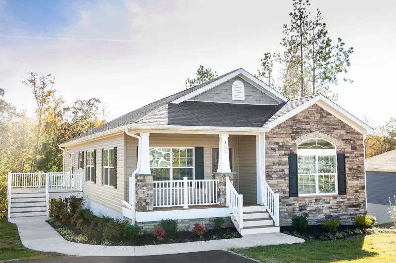 Exterior of a modular home featuring stone and tan siding, white trim and a front and side porch.