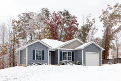 A snowy scene of a house with blue siding and attached garage.