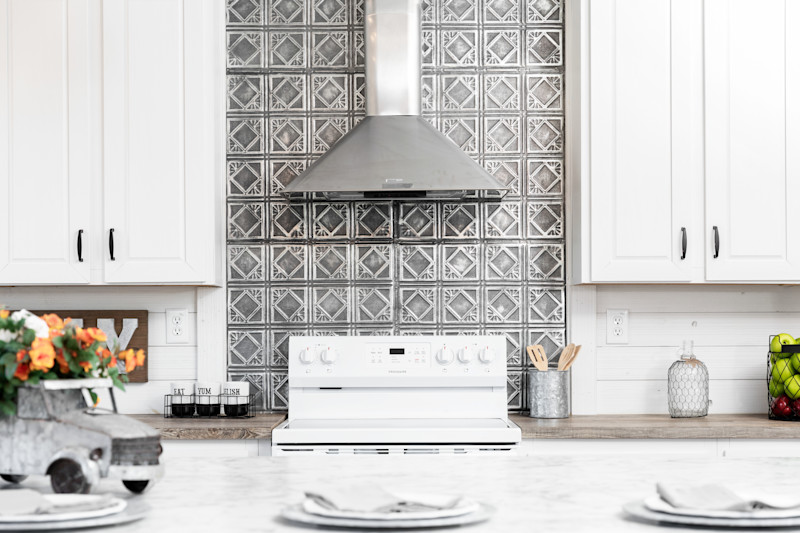 A kitchen in a manufactured home with tin backsplash tile behind the stove and white cabinets and shiplap walls