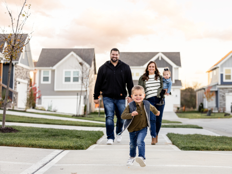 A little boy runs ahead of his family on the sidewalk of a neighborhood.