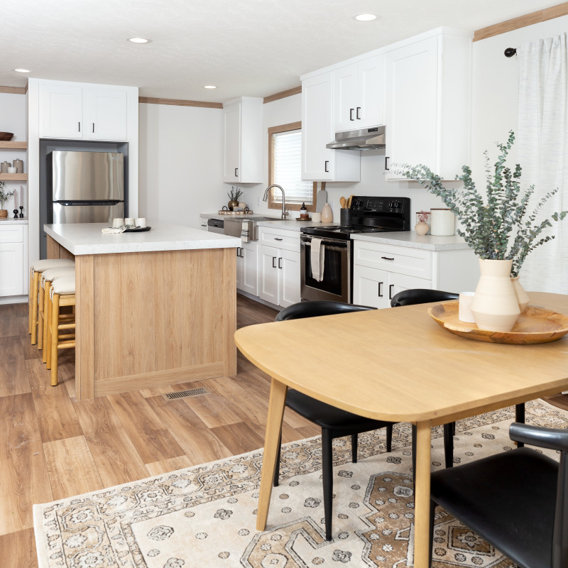 A modern farmhouse with white kitchen, white cabinets and natural oak finishes. Large island and open floor plan dining room area. Natural wood kitchen dining set and inset kitchen lights.