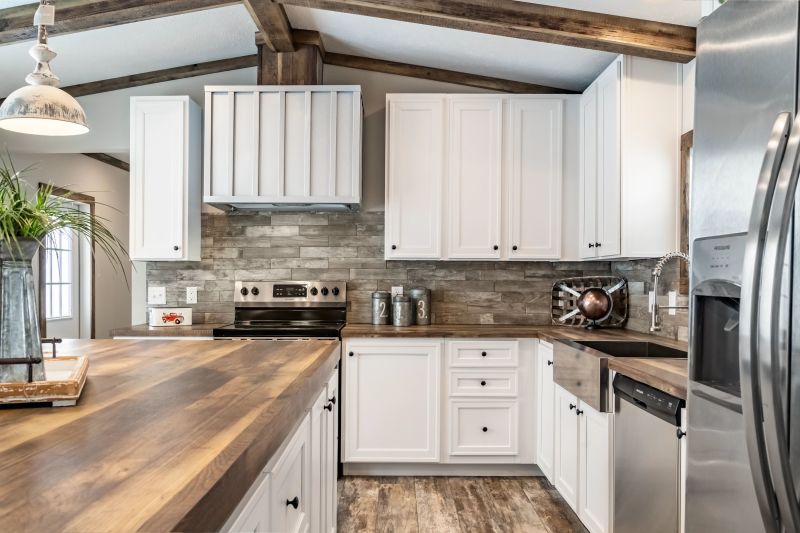 Farmhouse style manufactured home kitchen with wood-style countertops, white cabinets, stainless steel appliances and feeling beams