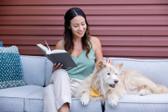 Woman reading outside on a couch and petting her dog. 