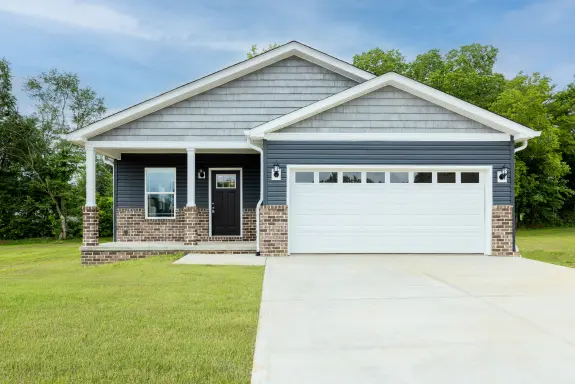 The [model name]'s highlights are this exterior with an attached garage and a front porch, along with a spa-inspired primary bathroom and a sleek kitchen inside.