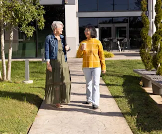 Two Clayton employees walk on an outdoor path carrying coffees.