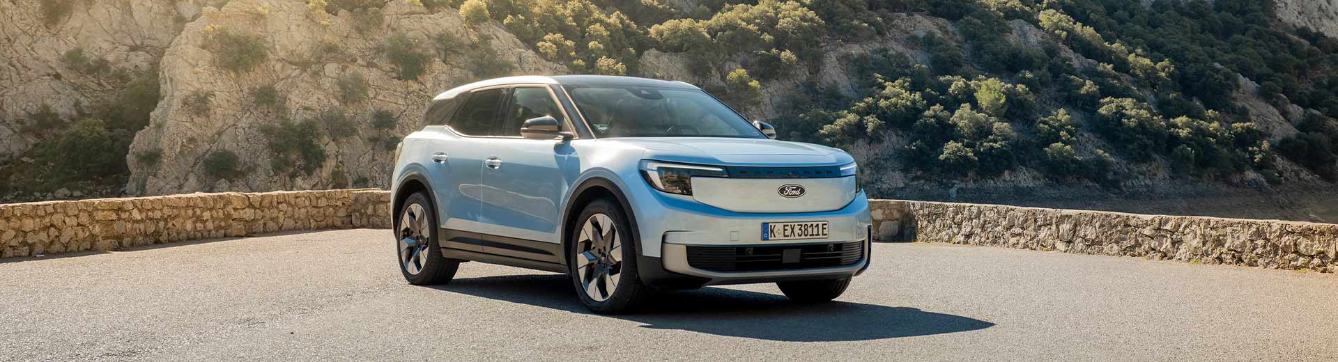 En-ljusblå-Ford-Explorer-elbil-parkerad-på-en-utsiktsplats-med-dramatiska-berg-och-ett-sjölandskap-i-bakgrunden