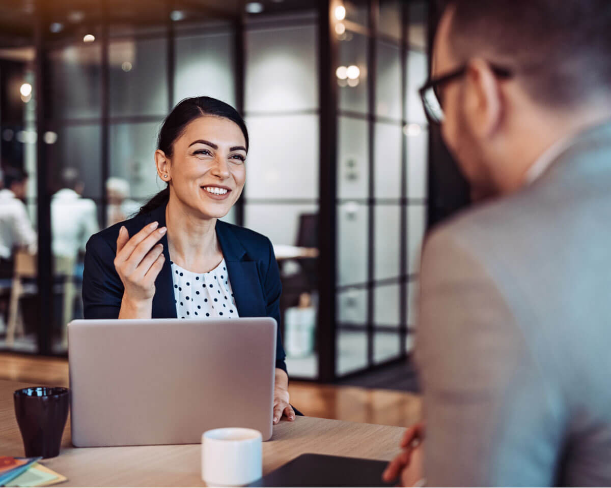 Two professionals in business attire, with cups of coffee and an open laptop nearby, have a job interview in an office setting