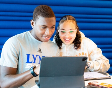 Two Lynn students looking at a tablet screen while surrounded by books