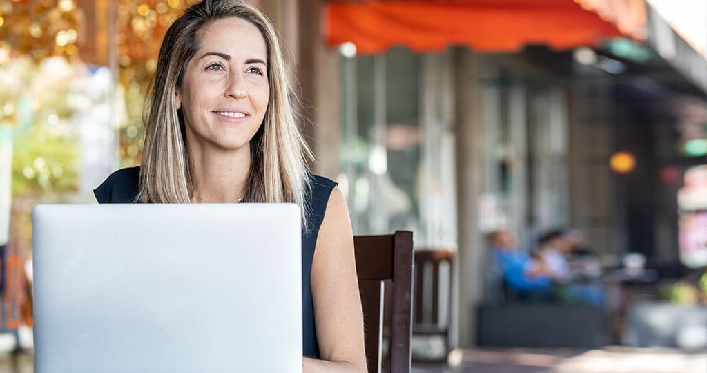 Smiling student working on a laptop outside a store