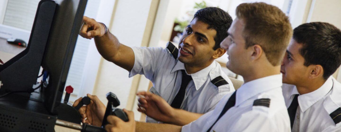 Group of aviation students in uniform looking at a computer