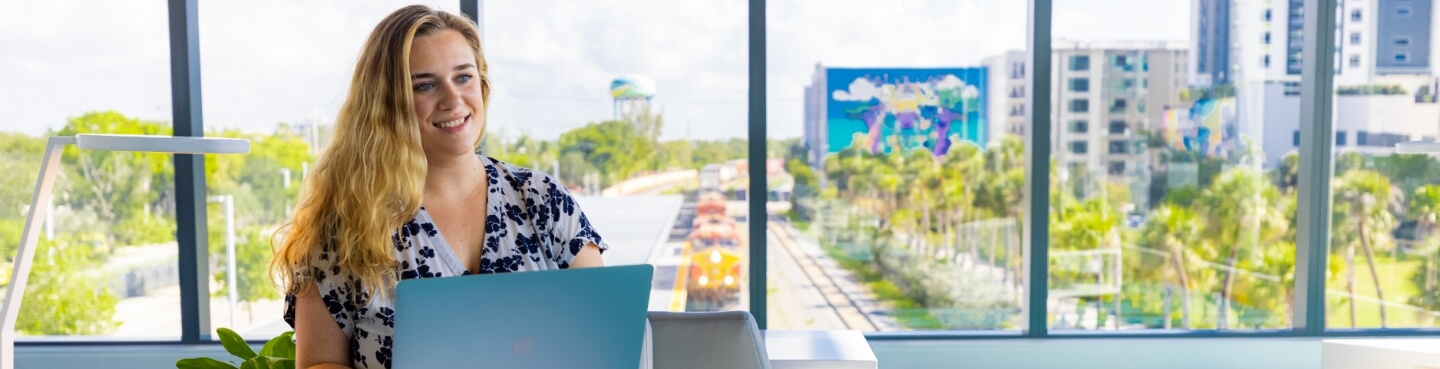 Lynn student working on a laptop in front of a large window overlooking train tracks