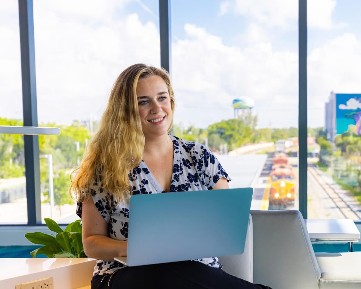 Lynn student working on a laptop in front of a large window overlooking train tracks