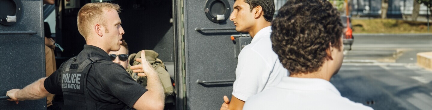 Police officer in bullet-proof vest standing outside a law enforcement van and talking to students