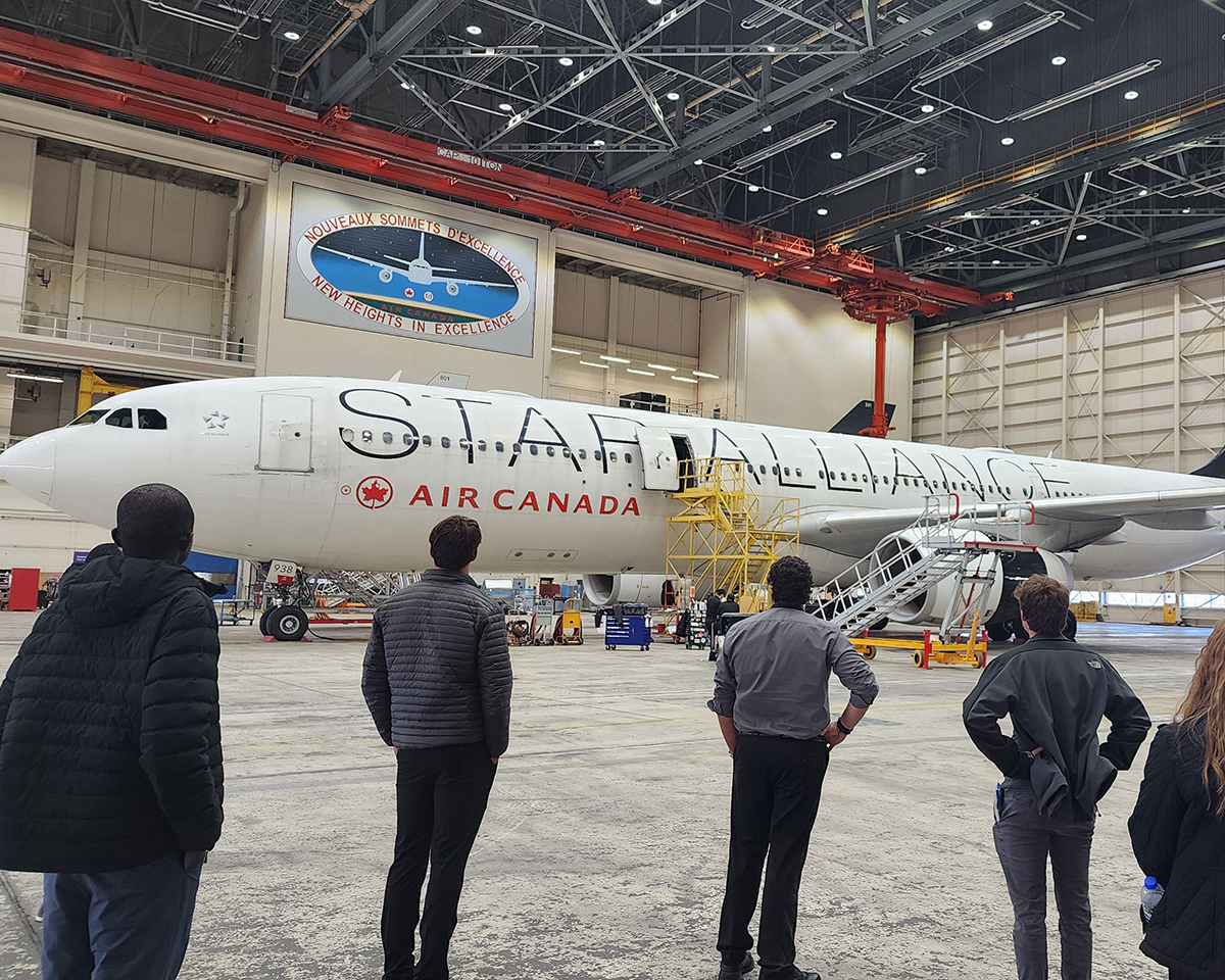 Several people standing in an airplane hangar, viewing a jet airplane