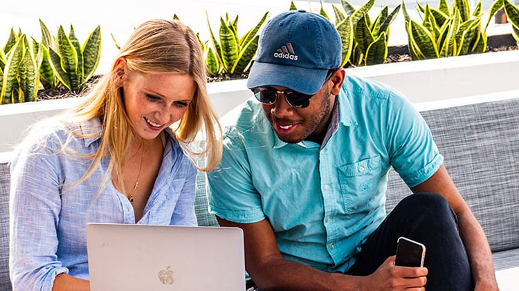 Two Lynn students sit outside together and look at a laptop.