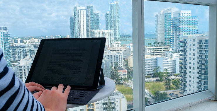 A student prepares to type on a tablet, with a view of South Florida outside the window.
