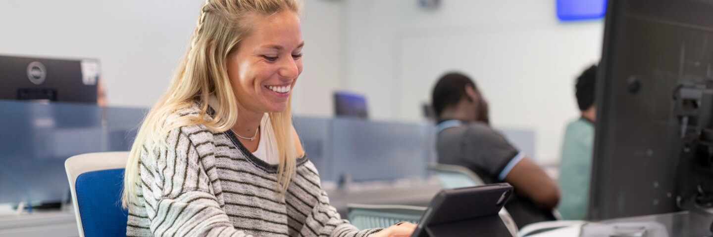 Young female student in a striped shirt working on a computer in a classroom.