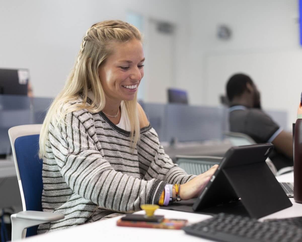Female Lynn student in a striped shirt working on a laptop in a classroom.
