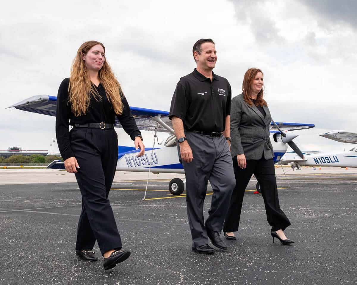 Three Lynn aviation professionals walking in an airfield with airplanes in the background