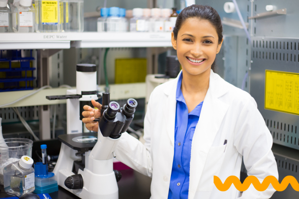 Female scientist in lab coat with microscope, happy, smiling at camera