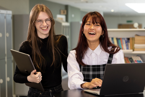 two girls in a college library, laughing while using the computer 