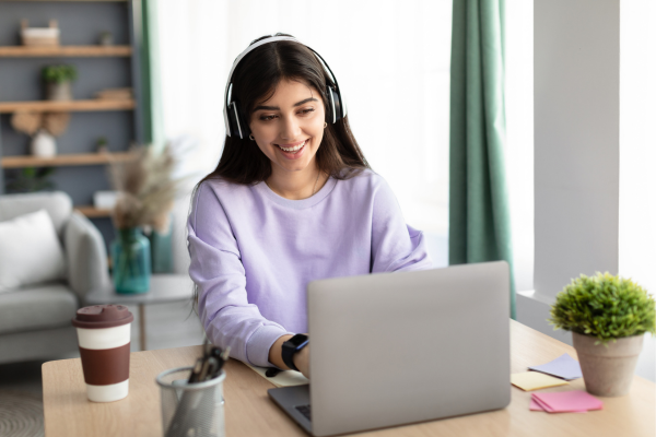 Young woman on laptop, smiling, with headphones on