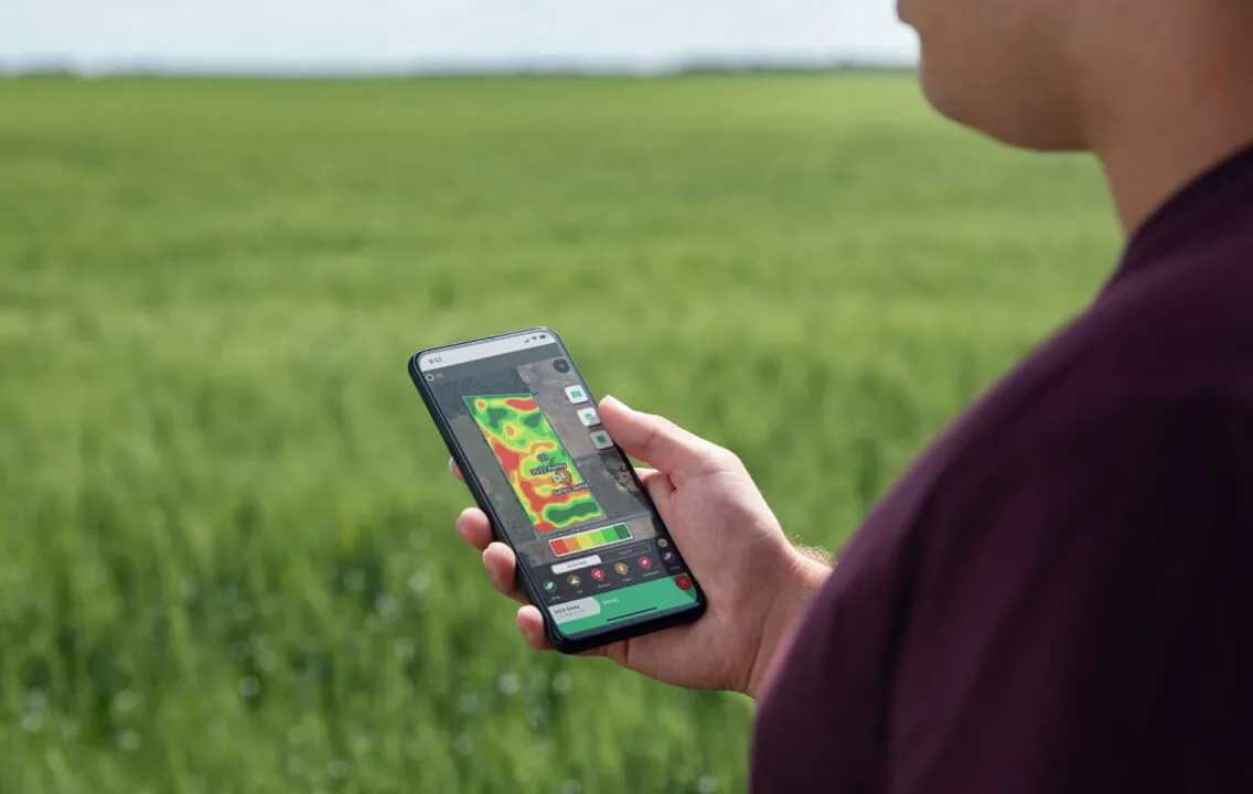 A man in front of a field holding a smartphone showing geo-referenced data