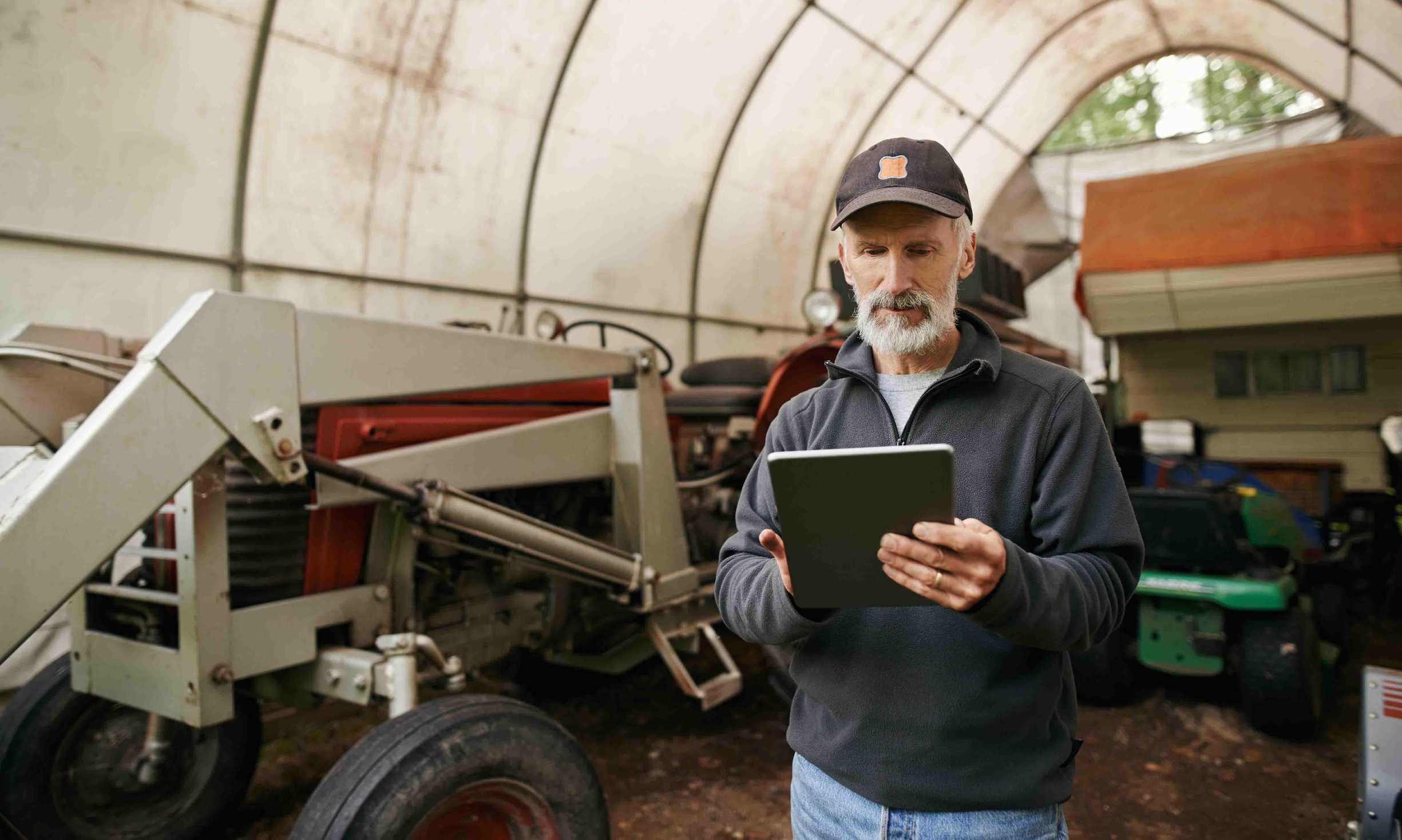 Farmer using a tablet to access an agriculture data API in front of a tractor.