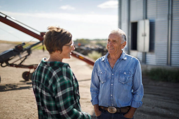 Un homme et une femme discutent de stratégies devant un silo céréalier, soulignant le rôle de l’agriculture numérique dans la production des cultures.

