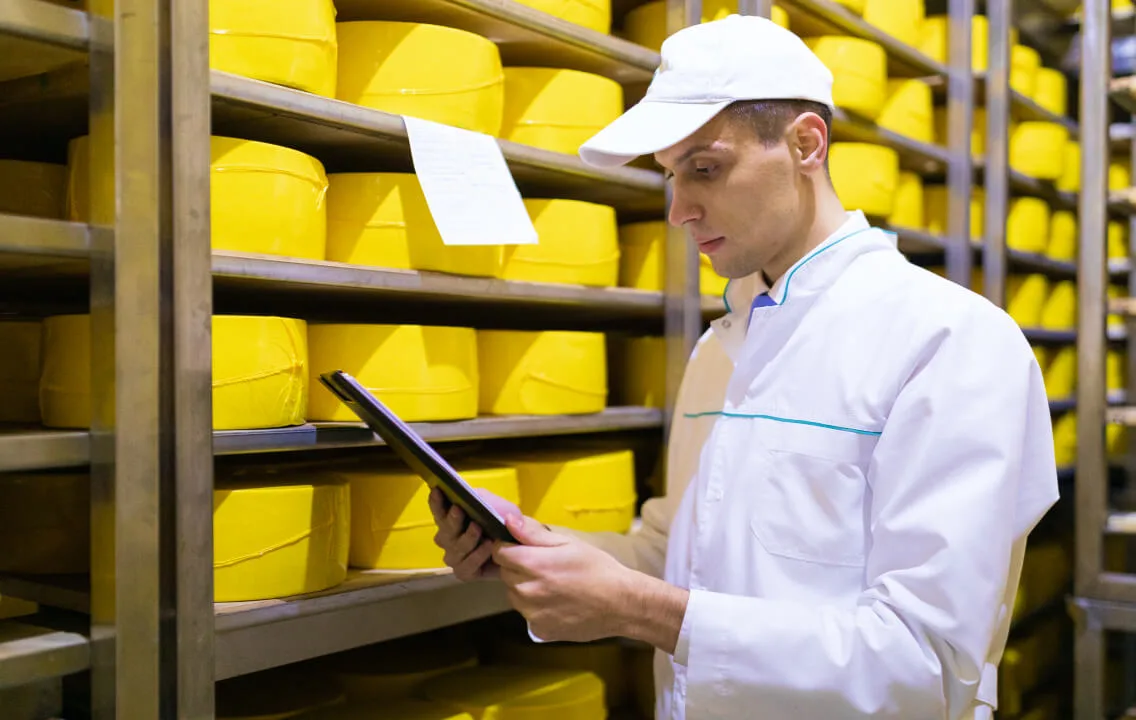 A man is using a tablet in a cheese warehouse.